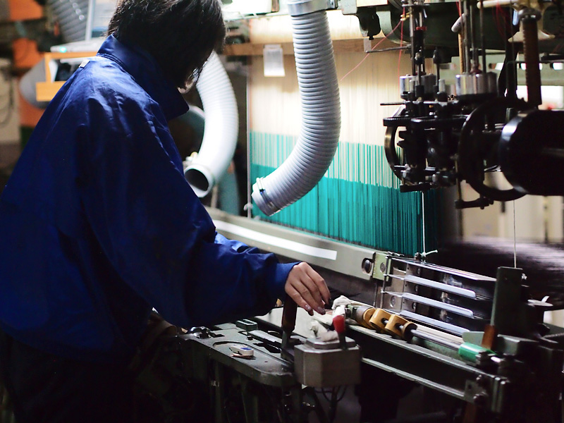 写真：織機のレバーを握る若い女性の職人
